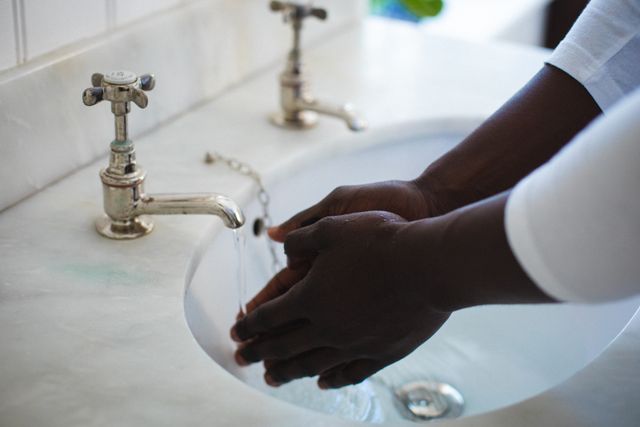This image depicts an African American man washing his hands in a bathroom sink, emphasizing hygiene and cleanliness. It can be used in articles or advertisements related to personal care, health, and sanitation. Ideal for promoting handwashing campaigns, hygiene products, or educational materials on preventing the spread of viruses and bacteria.