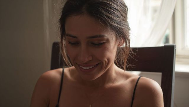 Intimate natural light portrait of woman smiling in spaghetti strap top by window