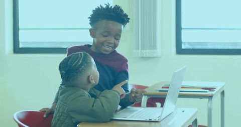 School children collaborating on laptop in bright classroom