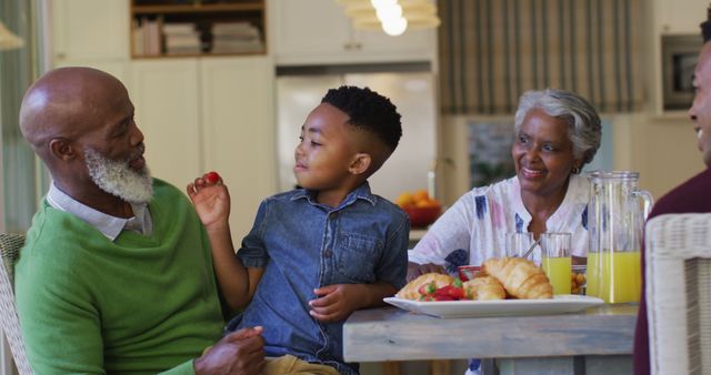 African american boy feeding strawberries to his grandfather while sitting on his lap at home. family, love and togetherness concept