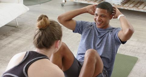 Partners doing sit-ups during home workout smiling man performing core crunches