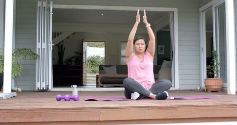 Mature woman practicing yoga and stretching on home deck with dumbbells and mat
