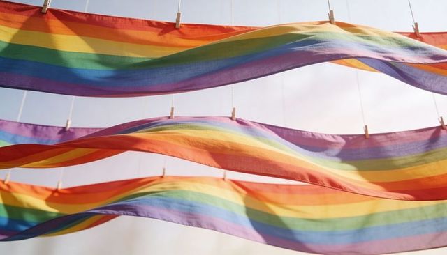 Billowing rainbow banners flowing across sunlit sky clipped to clotheslines with clothespins