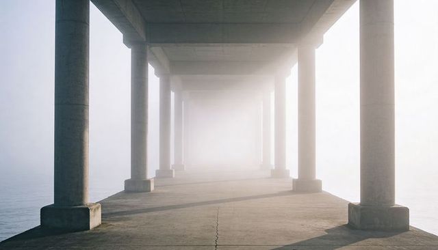 Leading concrete colonnade receding into fog over calm water, minimalist perspective
