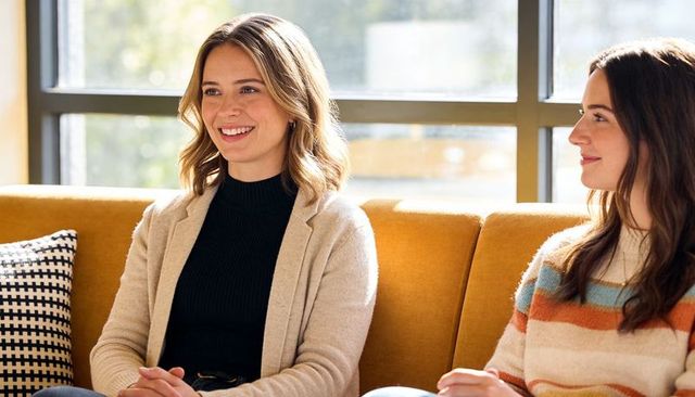 Women smiling and chatting on mustard sofa, cozy casual conversation and friendship moment
