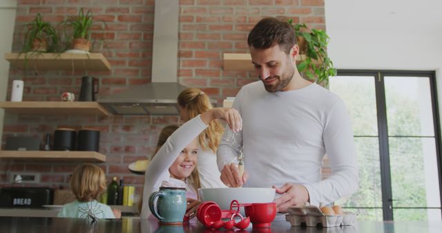 Happy family enjoying baking together in modern kitchen with lots of natural light. Parent instructing child while holding flour, two other children involved in background. Could be used in advertisements for family-oriented products, home cooking appliances, or culinary websites.