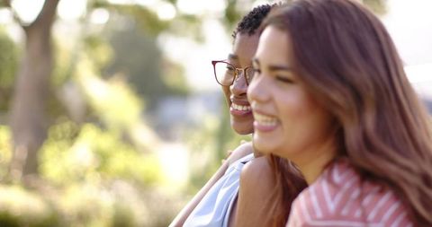 Smiling diverse women enjoying sunny park moment, laughing together in warm backlight