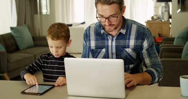 Father Working on Laptop and Son Using Digital Tablet in Living Room - Download Free Stock Images Pikwizard.com