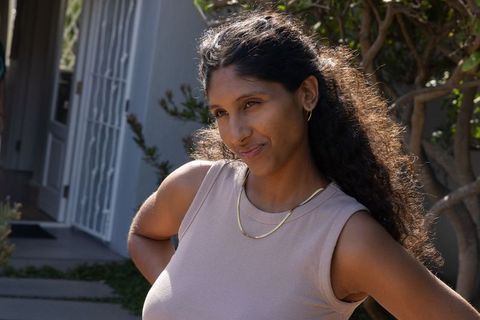 Sunlit african american woman standing on porch wearing gold necklaces and smiling