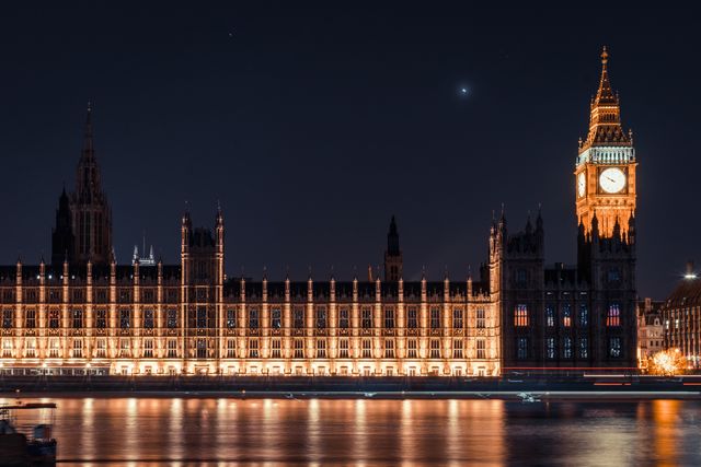 Night view of Big Ben and the Houses of Parliament lit up against the dark sky, reflecting in the River Thames. Excellent for travel websites, articles about London's landmarks, architecture studies, and promotional materials for tours in the UK.