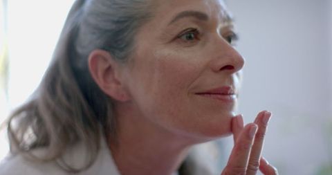 Mature woman gently applying skincare in natural light