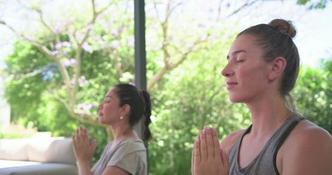 Multicultural women practicing mindful meditation and yoga breathwork on sunlit garden patio
