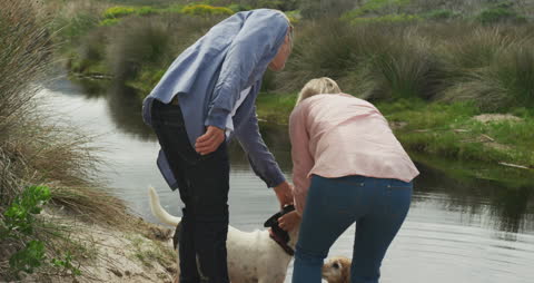Senior Couple Enjoying Fresh Air With Dog by Riverside