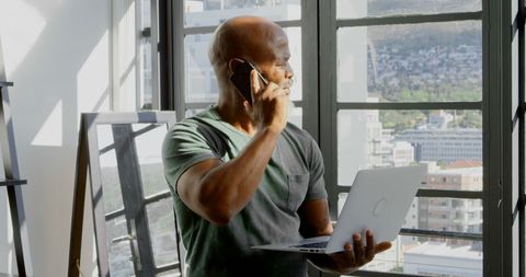 Senior Man Using Laptop and Talking on Smartphone at Home