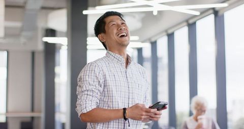 Smiling professional holding smartphone in modern office environment
