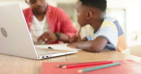 African american father tutoring son at kitchen table with laptop home learning moment