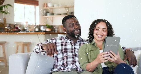 Couple Sharing Tablet on Couch in Bright Kitchen Relaxing Together with Digital Network Overlay