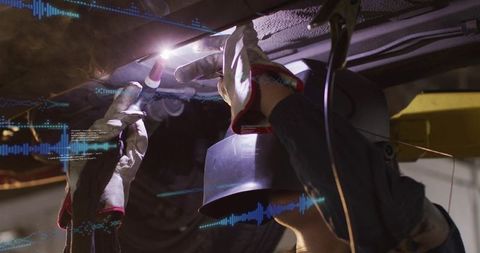 Female mechanic welding undercarriage with TIG torch and protective hood in garage