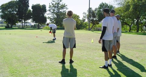 Male teammates training on grass field with cones and ball practicing teamwork and fitness