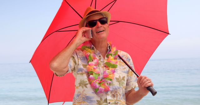 Smiling Elderly Man in Hawaiian Shirt Chatting on Phone, Holding Red Umbrella at Beach - Download Free Stock Images Pikwizard.com