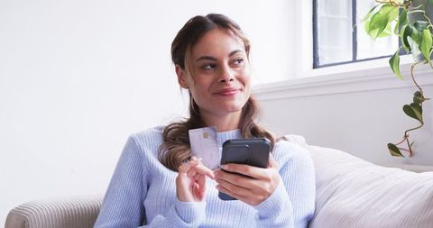 Woman shopping online with smartphone on comfortable couch