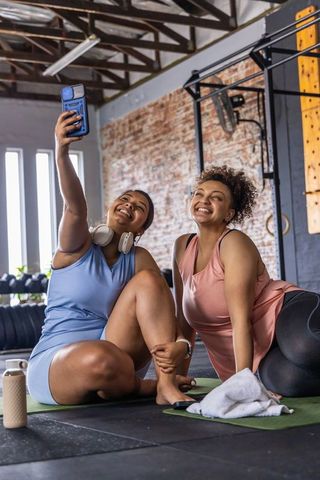 Two friends taking selfie on yoga mats after gym workout with headphones and kettlebells