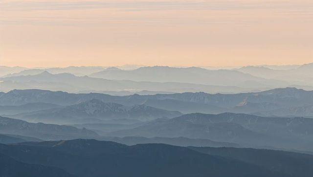 Pastel dawn layered alpine ridges mist-filled mountain panorama evoking calm serenity vista