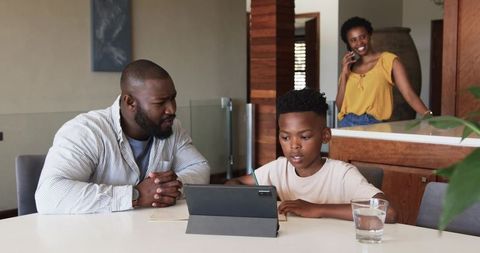 African American family doing homework together with tablet at modern dining table