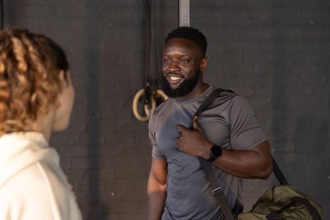 Smiling athlete carrying duffel bag greeting friend by gym rings in industrial gym