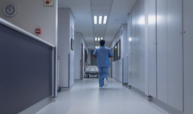 Rear view of male doctor running in the corridor at hospital