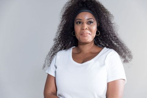 Confident african american woman posing in studio wearing white ribbed top and gold hoops