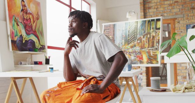 Thoughtful Artist Sitting in Studio Surrounded by Colorful Paintings - Download Free Stock Images Pikwizard.com