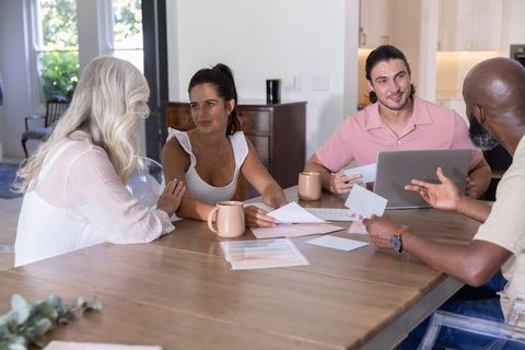 Diverse multi-generation family discussing finances and plans at dining table with laptop and docume