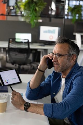 Midlife professional on call reviewing business analytics on tablet in modern office