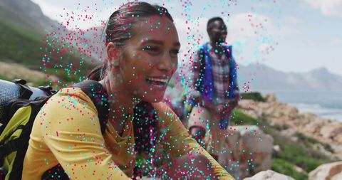 Smiling hiker sitting on coastal mountain trail overlooking ocean with companion and backpacks