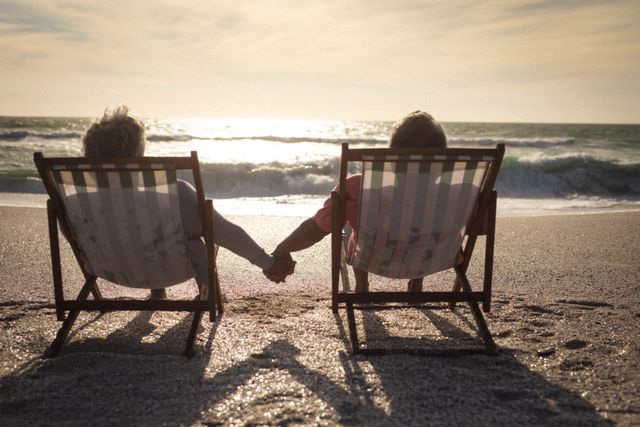 Rear view of senior couple holding hands while relaxing on folding chairs at beach during sunset. lifestyle, love and weekend.