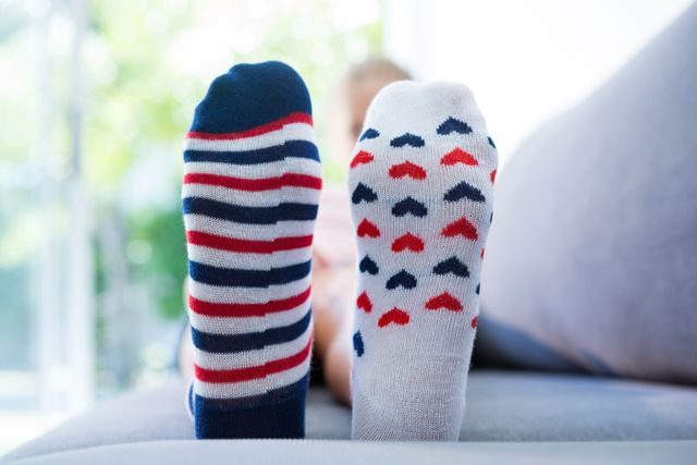 Close up of girl wearing different socks while sitting on sofa at home