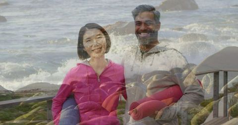 Smiling couple holding rolled yoga mats on seaside boardwalk with layered double exposure