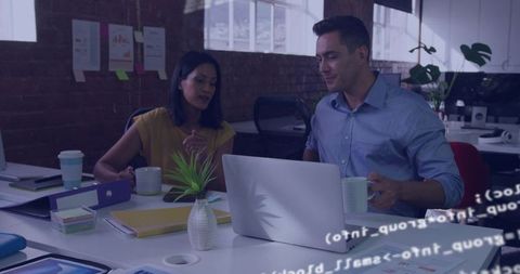 Two professionals collaborating over laptop in modern open-plan workspace team discussion