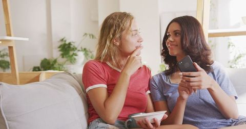 Two Women Relaxing on Sofa with Snacks and Smartphone at Home