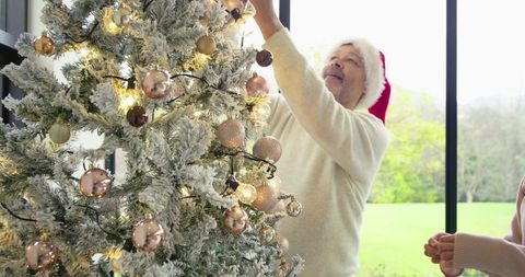 Mature Couple Decorating Flocked Christmas Tree with Rose Gold Baubles and Santa Hat