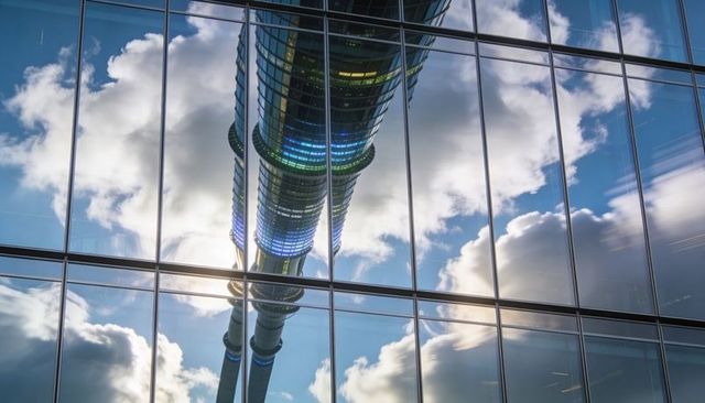 Glass curtain wall reflecting illuminated tower with led bands and cloud-filled sky grid