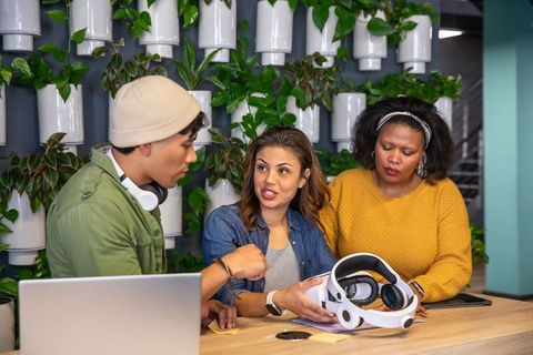 Diverse team testing vr headset and collaborating at coworking workspace with greenery