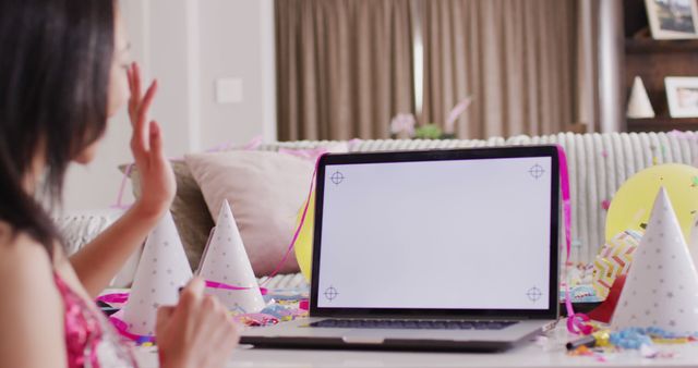 Woman participating in a virtual birthday party celebration via video call, sitting at home with laptop and festive decorations. Ideal for topics on online celebrations, social distancing, remote interaction, digital events, and using technology to stay connected with loved ones.