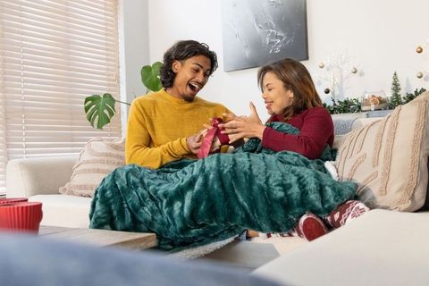 Couple exchanging holiday gift on sofa cuddling under blanket with cozy living room decor