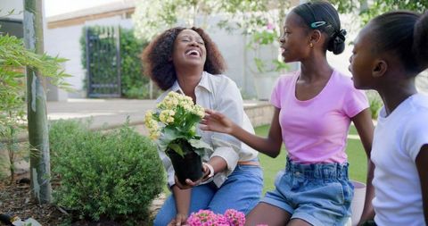 Mother laughing and gardening with daughters while holding flowering pot in backyard