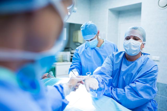 Surgeons wearing blue surgical gowns, masks, and gloves, performing an operation in a hospital operating room. Ideal for use in healthcare publications, medical websites, blogs discussing surgical procedures, and educational materials for medical students.