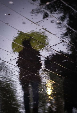 Reflective silhouette with umbrella in rain puddles