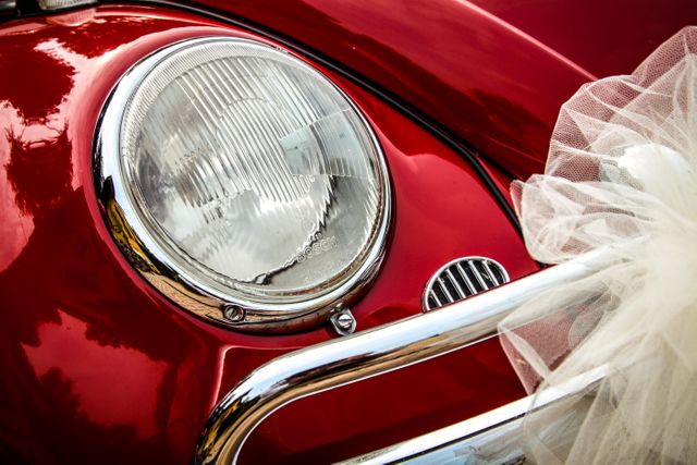 This nostalgic image shows a close-up of a vintage red car's headlight paired with elegant wedding decoration. Perfect for websites or promotional materials focused on classic cars, weddings, nostalgia, or vintage automobile enthusiasts. Ideal for wedding blogs, automotive content, or thematic photo collections.