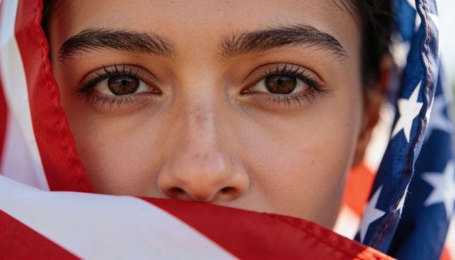 Adolescent female gazing through draped american flag closeup portrait